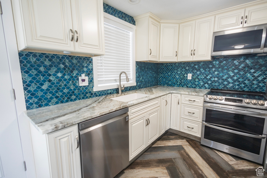 Kitchen with appliances with stainless steel finishes, a sink, light stone countertops, and tasteful backsplash