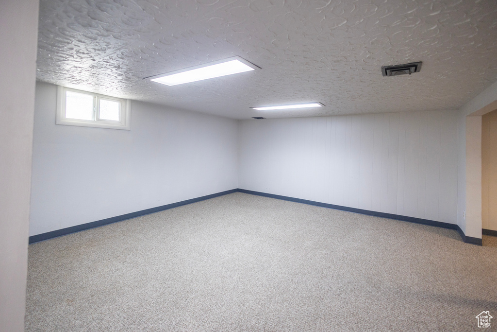 Empty room with a textured ceiling, carpet floors, and baseboards