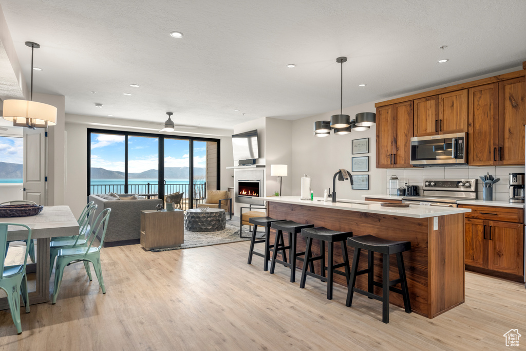 Kitchen featuring stainless steel appliances, brown cabinets, a sink, light wood finished floors, and open floor plan