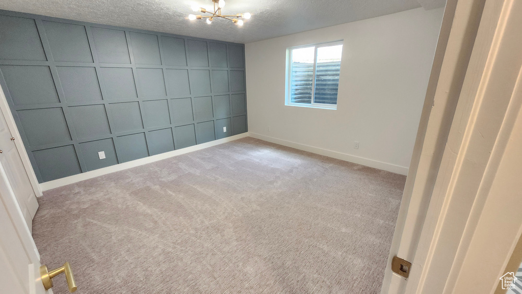Carpeted spare room featuring a decorative wall, a chandelier, baseboards, and a textured ceiling