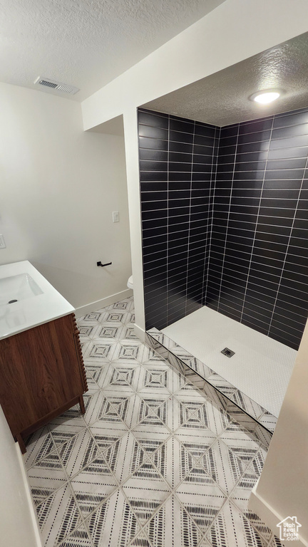 Bathroom with a textured ceiling, tiled shower, toilet, vanity, and baseboards