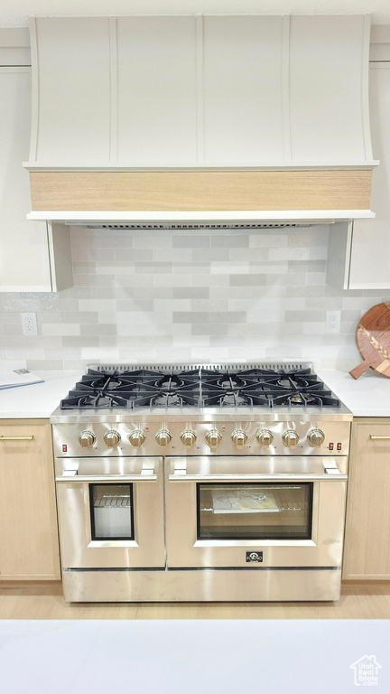 Kitchen featuring double oven range, light brown cabinetry, light countertops, and backsplash