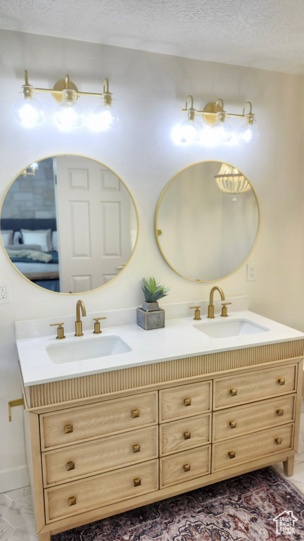 Full bathroom with double vanity, a textured ceiling, marble finish floors, and baseboards