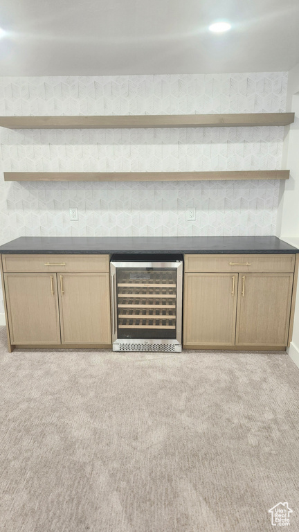 Indoor dry bar with wine cooler, light colored carpet, and baseboards