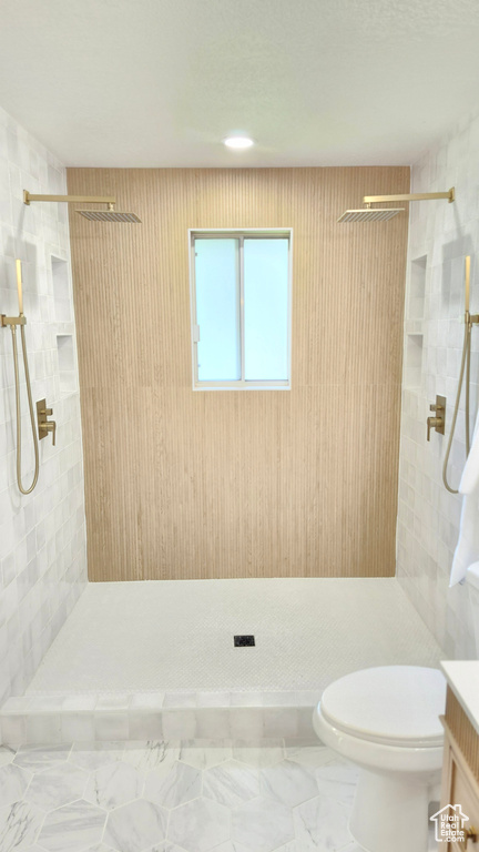 Bathroom with a tile shower, toilet, marble finish floors, and vanity