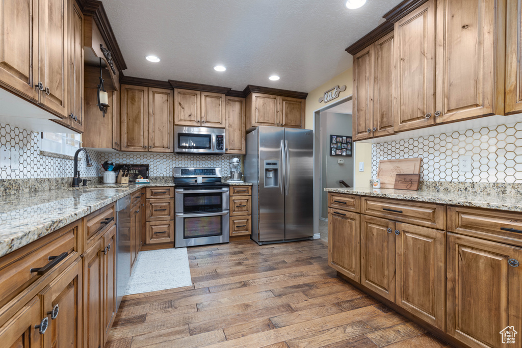 Kitchen with stainless steel appliances, a sink, wood finished floors, decorative backsplash, and recessed lighting