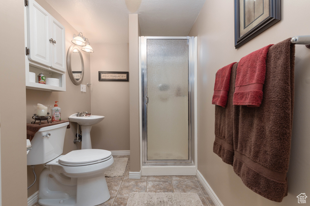 Bathroom with toilet, a shower stall, baseboards, and tile patterned flooring