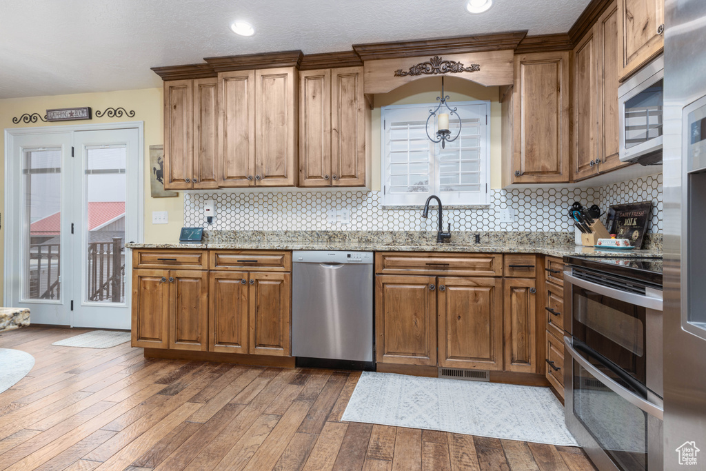 Kitchen featuring appliances with stainless steel finishes, a sink, light stone counters, dark wood-style flooring, and brown cabinetry