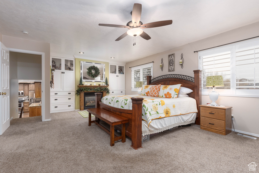 Bedroom with carpet flooring, a fireplace with flush hearth, ceiling fan, and baseboards