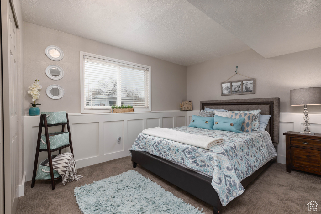Carpeted bedroom with a textured ceiling, a wainscoted wall, and a decorative wall