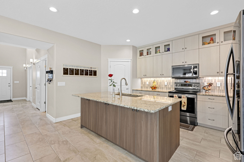 Kitchen featuring stainless steel appliances, a sink, an island with sink, tasteful backsplash, and light stone counters