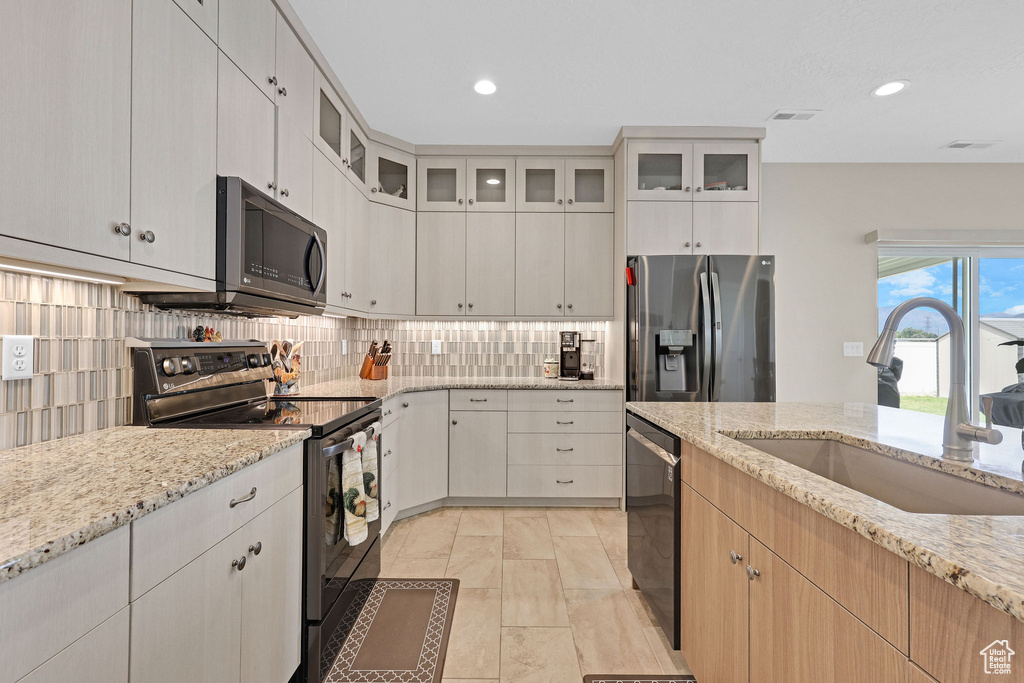 Kitchen with stainless steel appliances, a sink, decorative backsplash, light stone counters, and glass insert cabinets