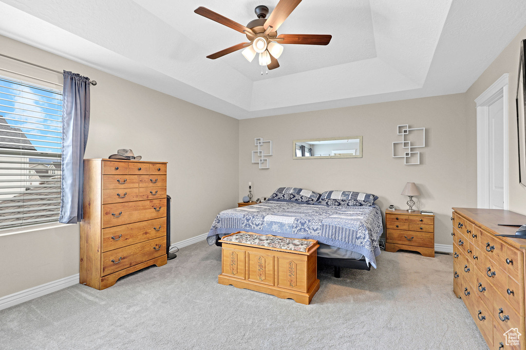 Bedroom with carpet floors, a tray ceiling, baseboards, and ceiling fan