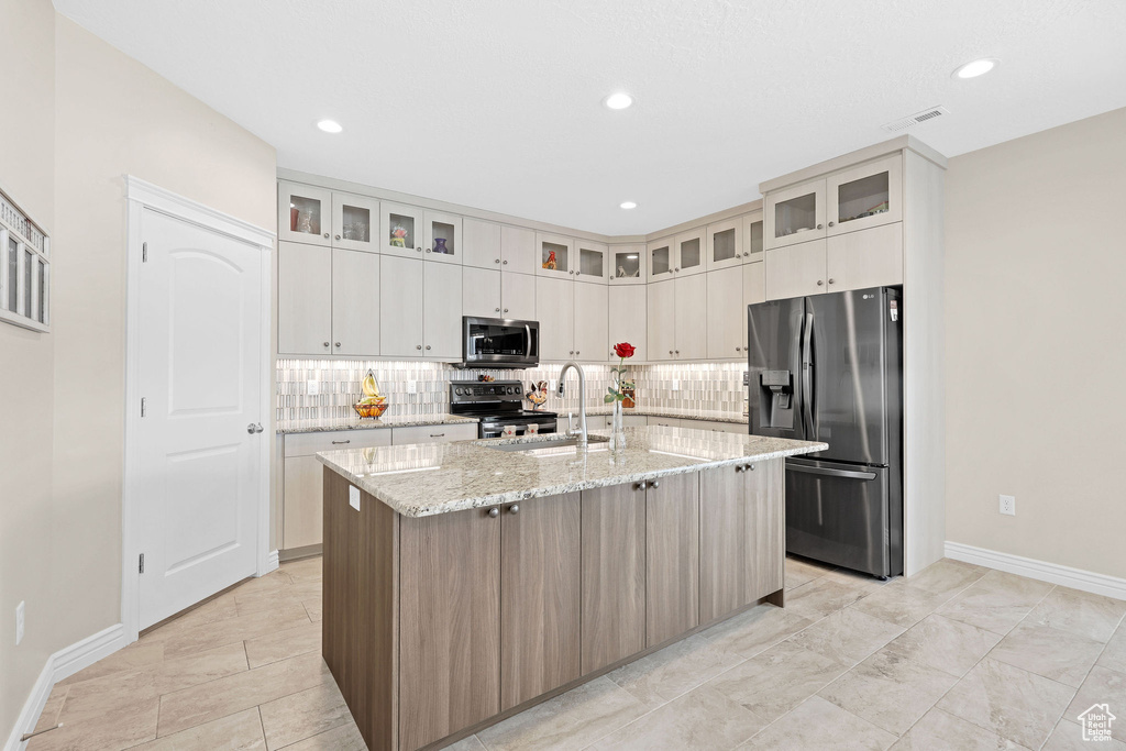 Kitchen with appliances with stainless steel finishes, a sink, baseboards, tasteful backsplash, and an island with sink