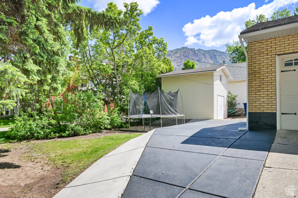 View of property exterior with a trampoline, brick siding, a mountain view, and a patio