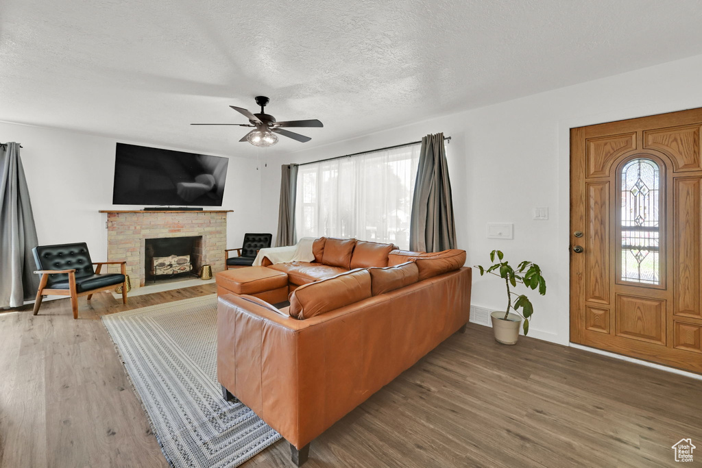 Living room with wood finished floors, a fireplace, ceiling fan, and a textured ceiling