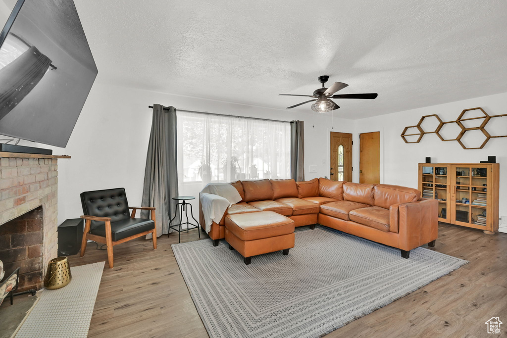 Living area featuring light wood finished floors, a ceiling fan, a brick fireplace, and a textured ceiling