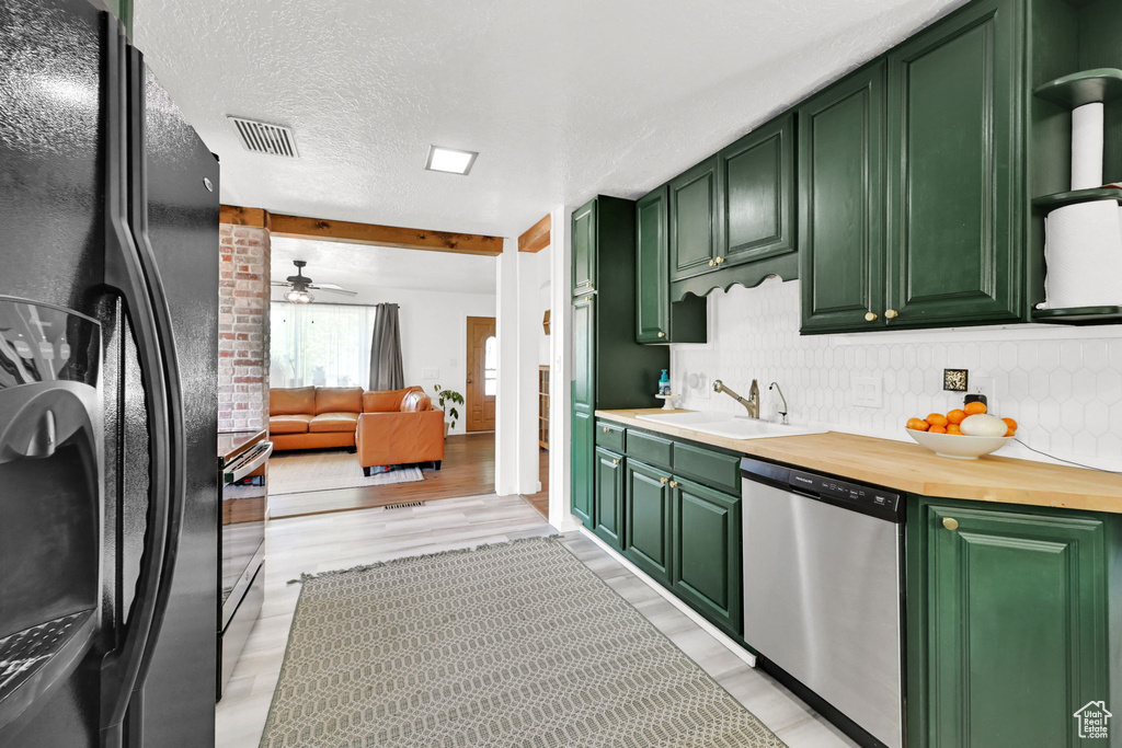 Kitchen featuring freestanding refrigerator, green cabinetry, stainless steel dishwasher, a sink, and decorative backsplash