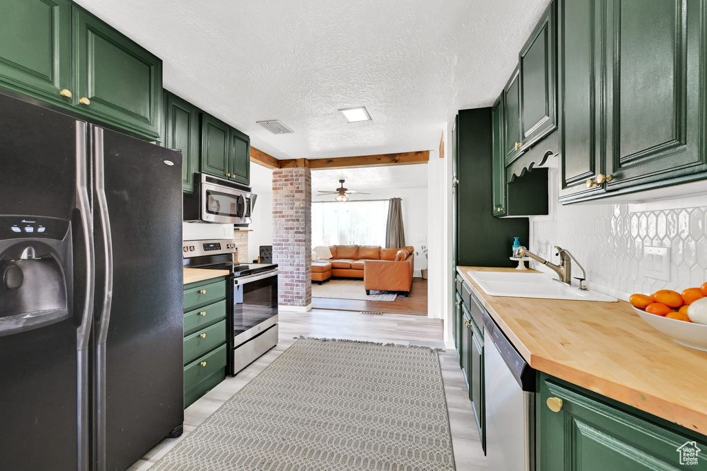 Kitchen featuring stainless steel appliances, green cabinets, a sink, and a textured ceiling