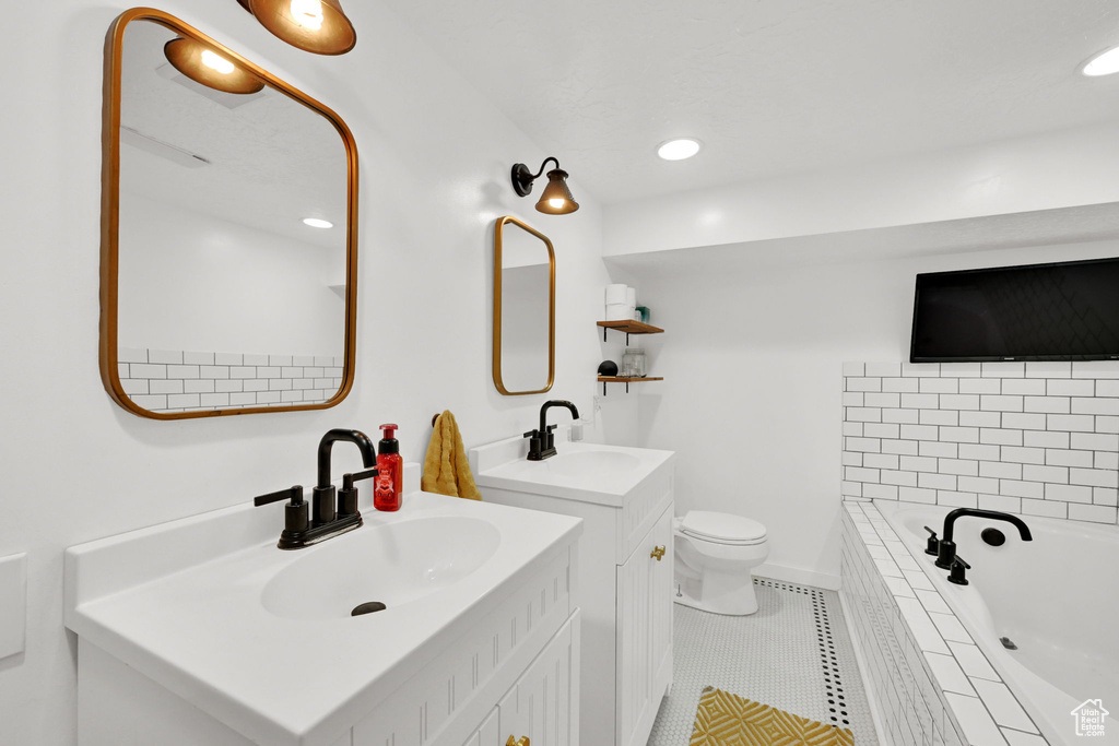 Bathroom with tiled tub, tile patterned floors, two vanities, toilet, and recessed lighting