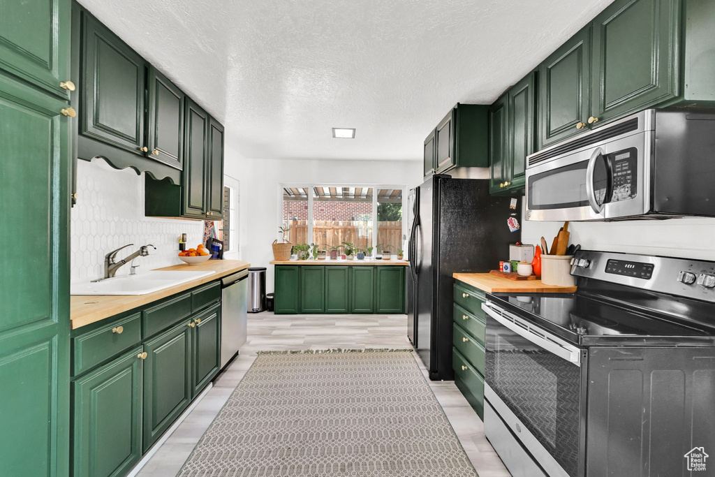 Kitchen with stainless steel appliances, green cabinets, a sink, light wood-style floors, and a textured ceiling