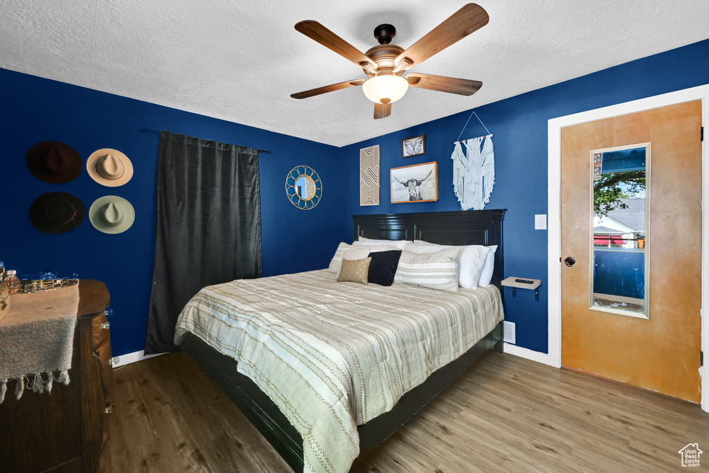 Bedroom with wood finished floors, baseboards, a textured ceiling, and a ceiling fan