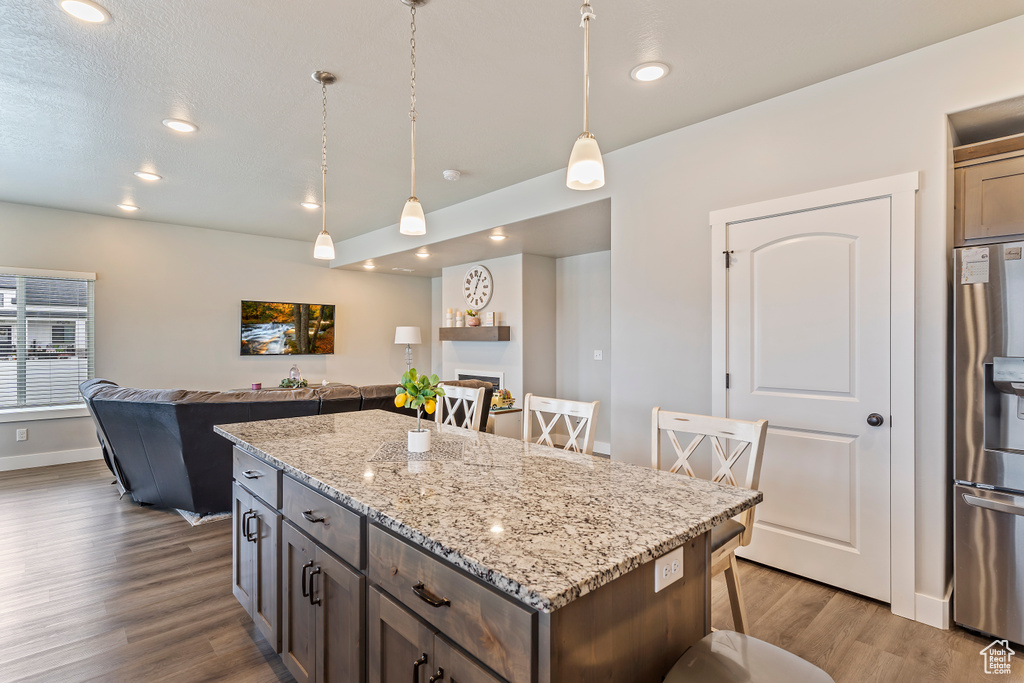 Kitchen featuring stainless steel fridge with ice dispenser, wood finished floors, pendant lighting, a kitchen island, and open floor plan