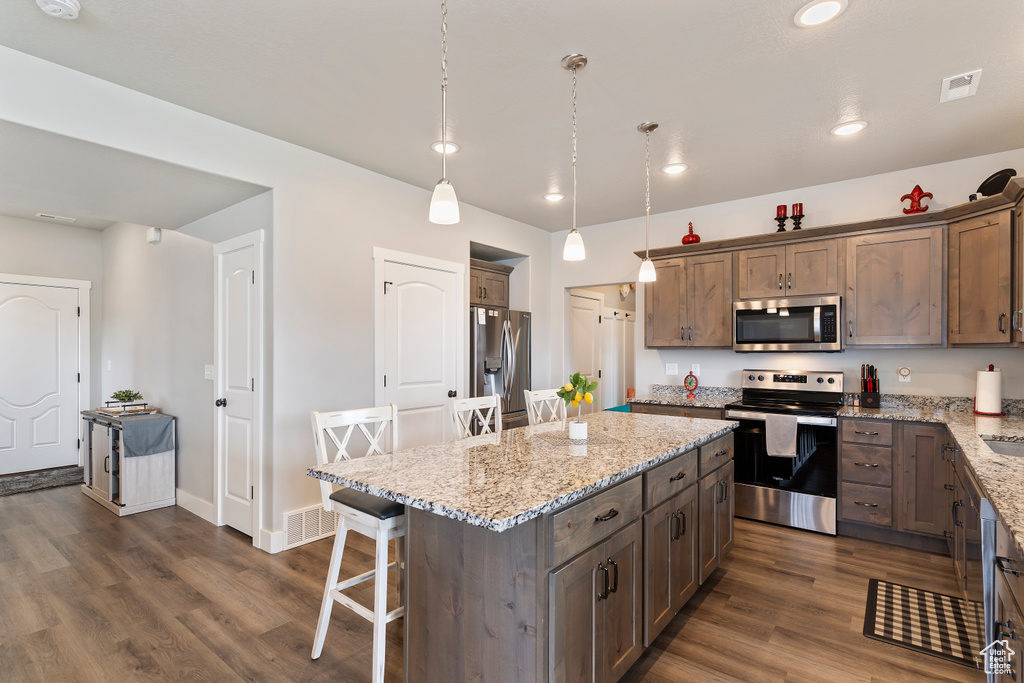 Kitchen with stainless steel appliances, a kitchen breakfast bar, light stone counters, dark wood finished floors, and recessed lighting