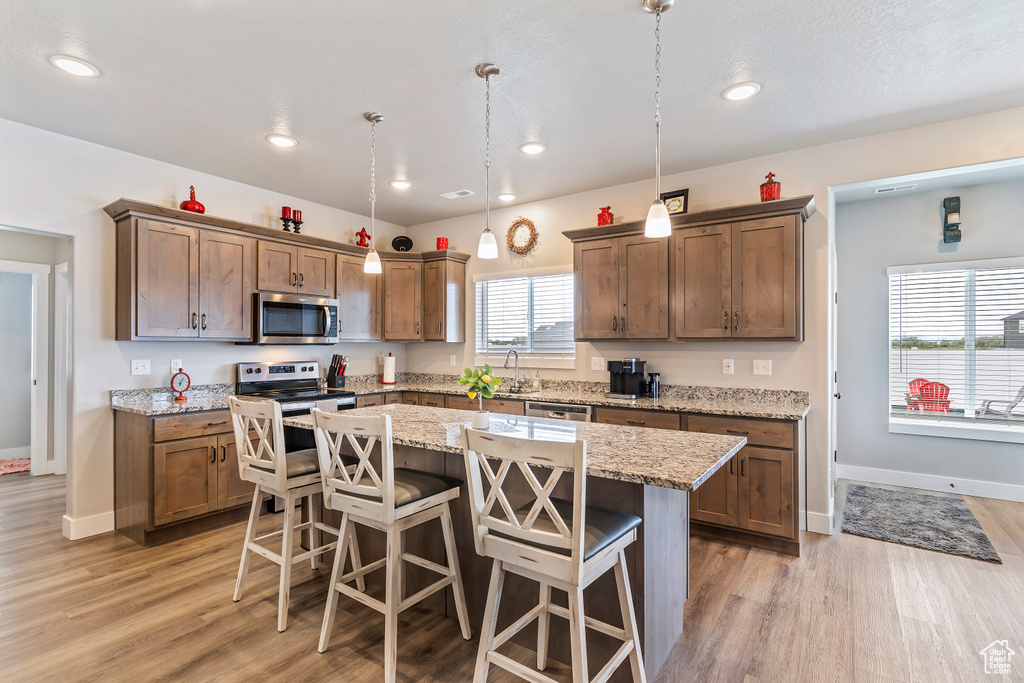 Kitchen with appliances with stainless steel finishes, light wood-style floors, a kitchen bar, a kitchen island, and baseboards