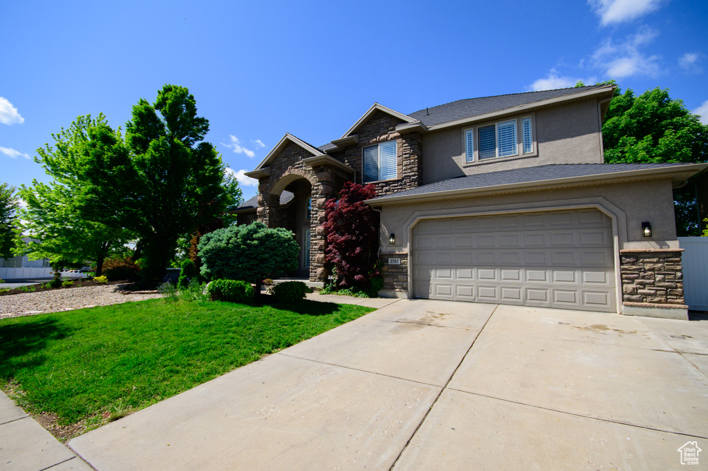 View of front of home with stone siding, stucco siding, driveway, and a front lawn