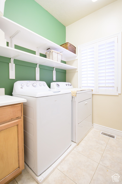 Laundry area with independent washer and dryer, light tile patterned floors, and baseboards