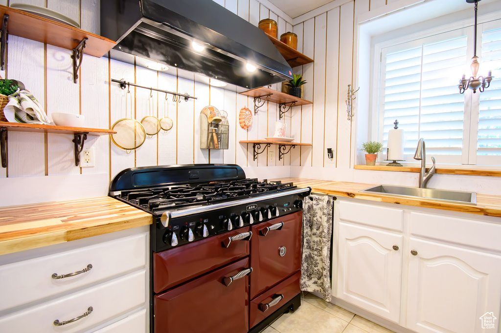 Kitchen featuring open shelves, a sink, exhaust hood, gas range, and butcher block counters