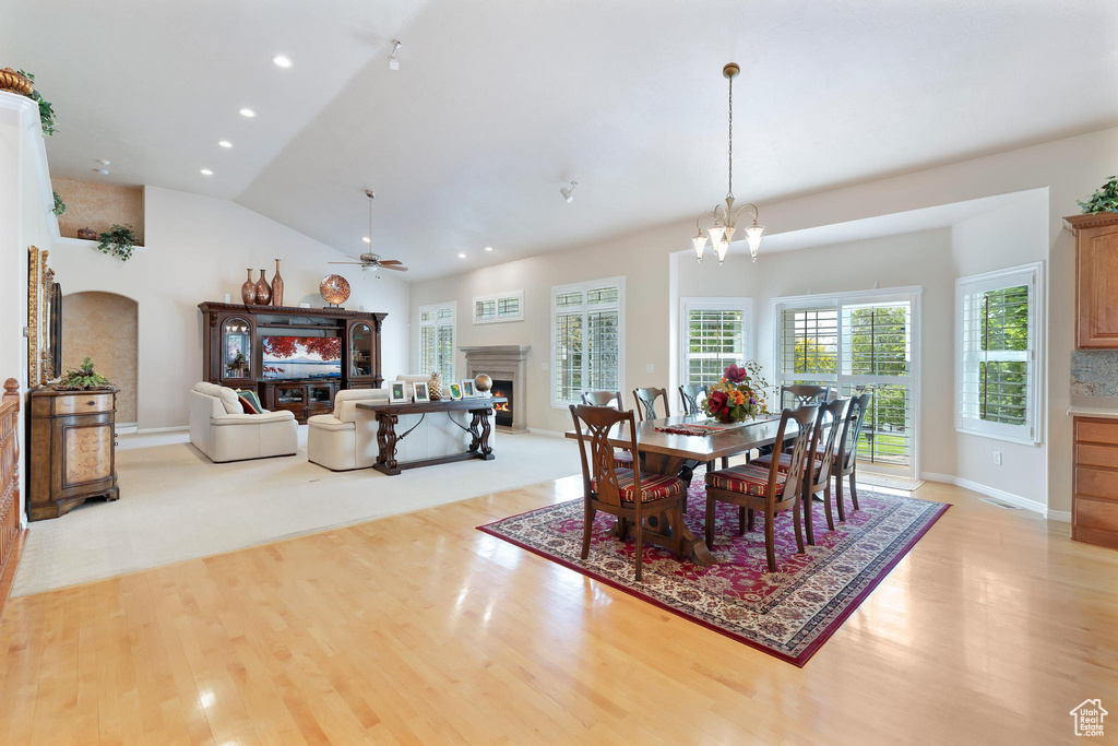 Dining space with light wood finished floors, a lit fireplace, a ceiling fan, recessed lighting, and vaulted ceiling