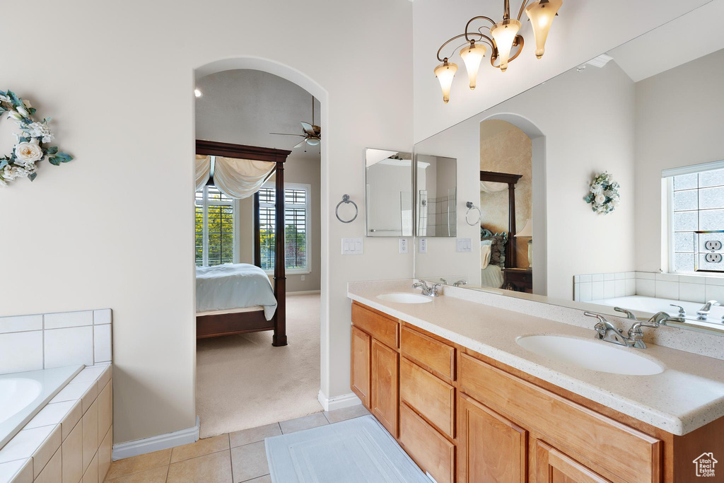 Ensuite bathroom with tile patterned floors, a ceiling fan, a bath, double vanity, and baseboards