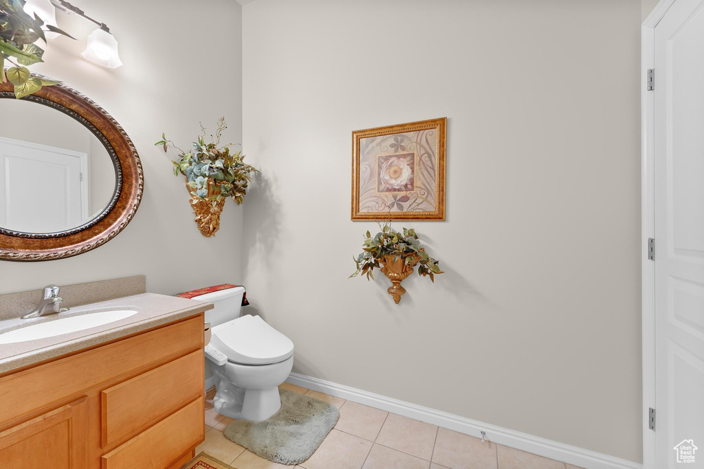 Half bathroom with vanity, toilet, tile patterned floors, and baseboards