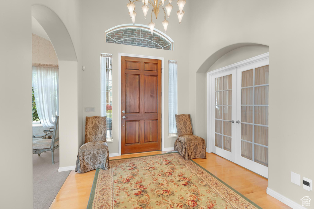 Foyer with wood finished floors, arched walkways, french doors, a towering ceiling, and baseboards