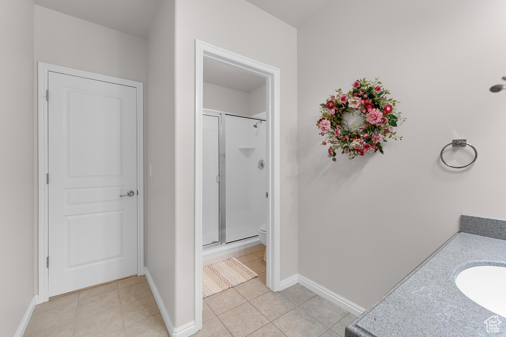 Bathroom with a stall shower, tile patterned floors, toilet, baseboards, and a sink