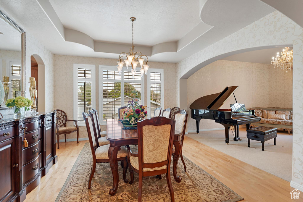 Dining area featuring wallpapered walls, a chandelier, arched walkways, light wood finished floors, and baseboards