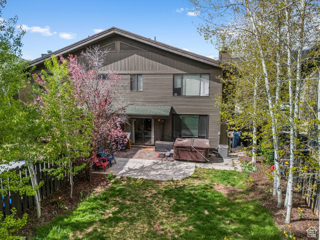 Back of house featuring a hot tub, a patio, a lawn, and a chimney