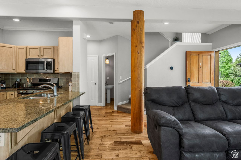 Kitchen featuring appliances with stainless steel finishes, open floor plan, light wood finished floors, a sink, and backsplash