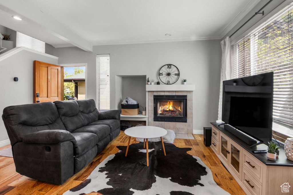 Living area featuring a tiled fireplace, light wood-type flooring, crown molding, baseboards, and beam ceiling
