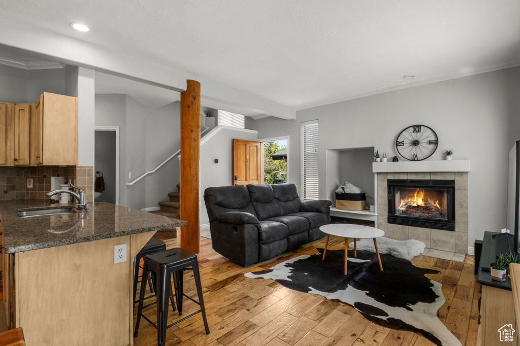 Living room with light wood finished floors, a tiled fireplace, stairs, crown molding, and recessed lighting