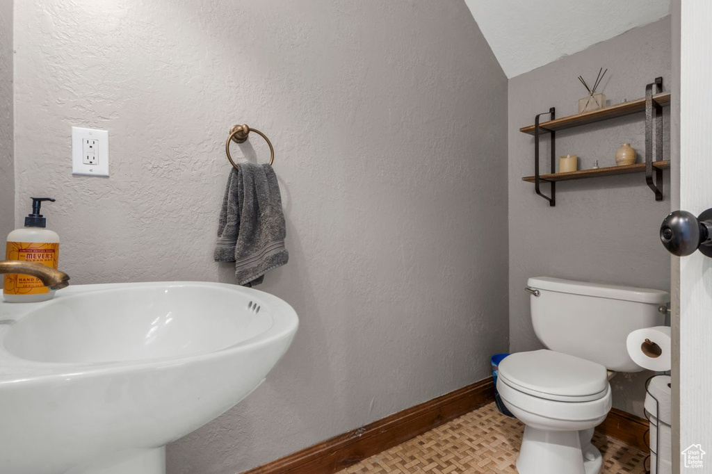 Bathroom featuring baseboards, a sink, toilet, and vaulted ceiling
