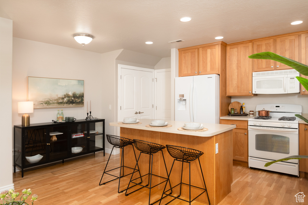 Kitchen featuring white appliances, light wood-style flooring, a kitchen breakfast bar, a center island, and recessed lighting