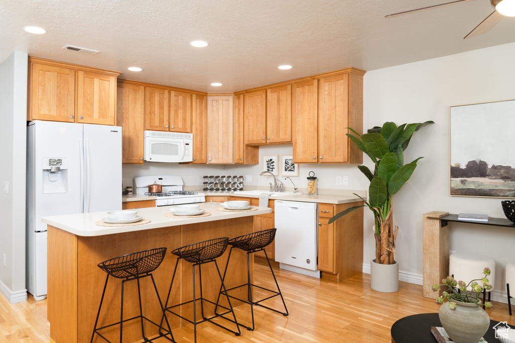 Kitchen with white appliances, light countertops, light wood finished floors, a kitchen breakfast bar, and recessed lighting