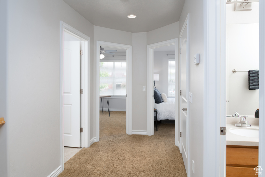 Hallway featuring a sink, light carpet, and baseboards