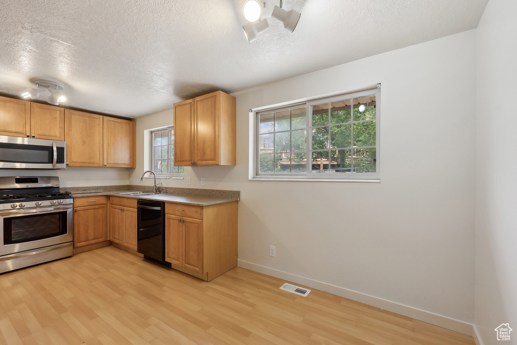 Kitchen with stainless steel appliances, light wood finished floors, a sink, a textured ceiling, and baseboards