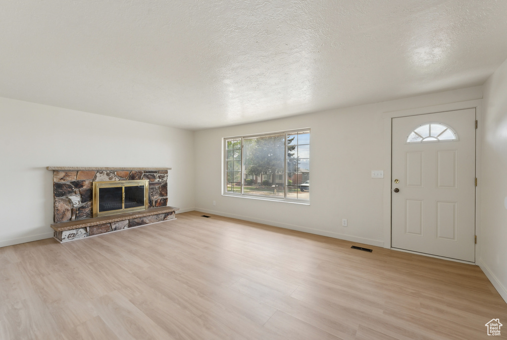 Unfurnished living room with light wood finished floors, a textured ceiling, baseboards, and a stone fireplace