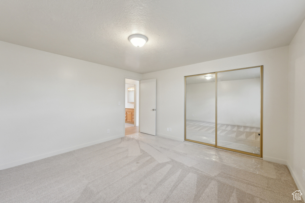 Unfurnished bedroom featuring light colored carpet, a closet, a textured ceiling, and baseboards