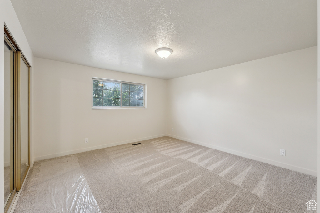 Unfurnished bedroom with light carpet, a closet, baseboards, and a textured ceiling
